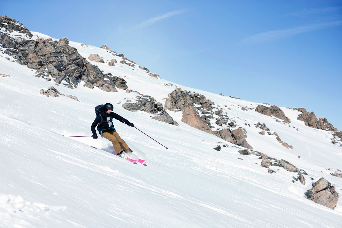 Person som står på ski i en bratt bakke på et snødekt fjell under klarblå himmel, perfekt for vintersport og eventyr